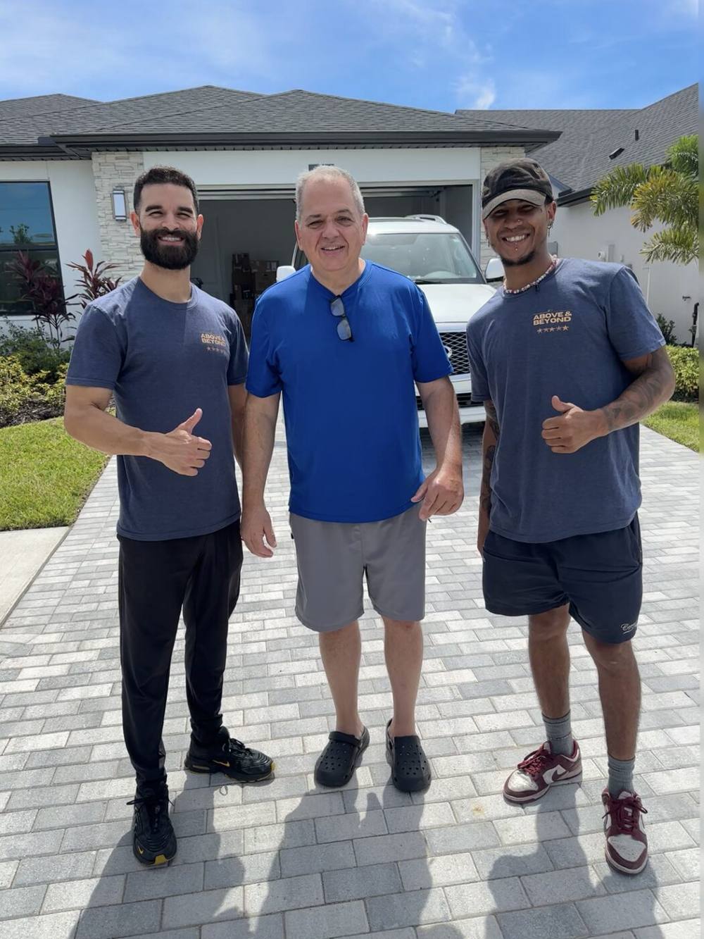Two Above&Beyond movers in branded shirts giving a thumbs-up beside a smiling customer in the driveway of a new Florida home