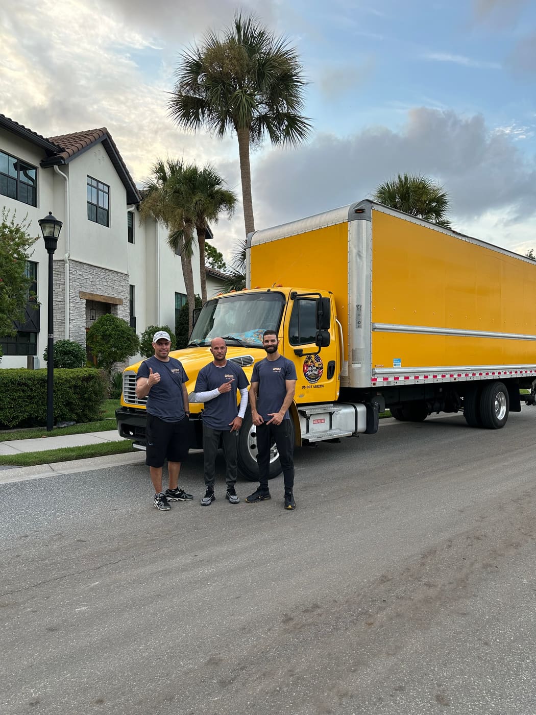 Three Above&Beyond movers in matching branded shirts standing in front of the company box truck outside a Florida home