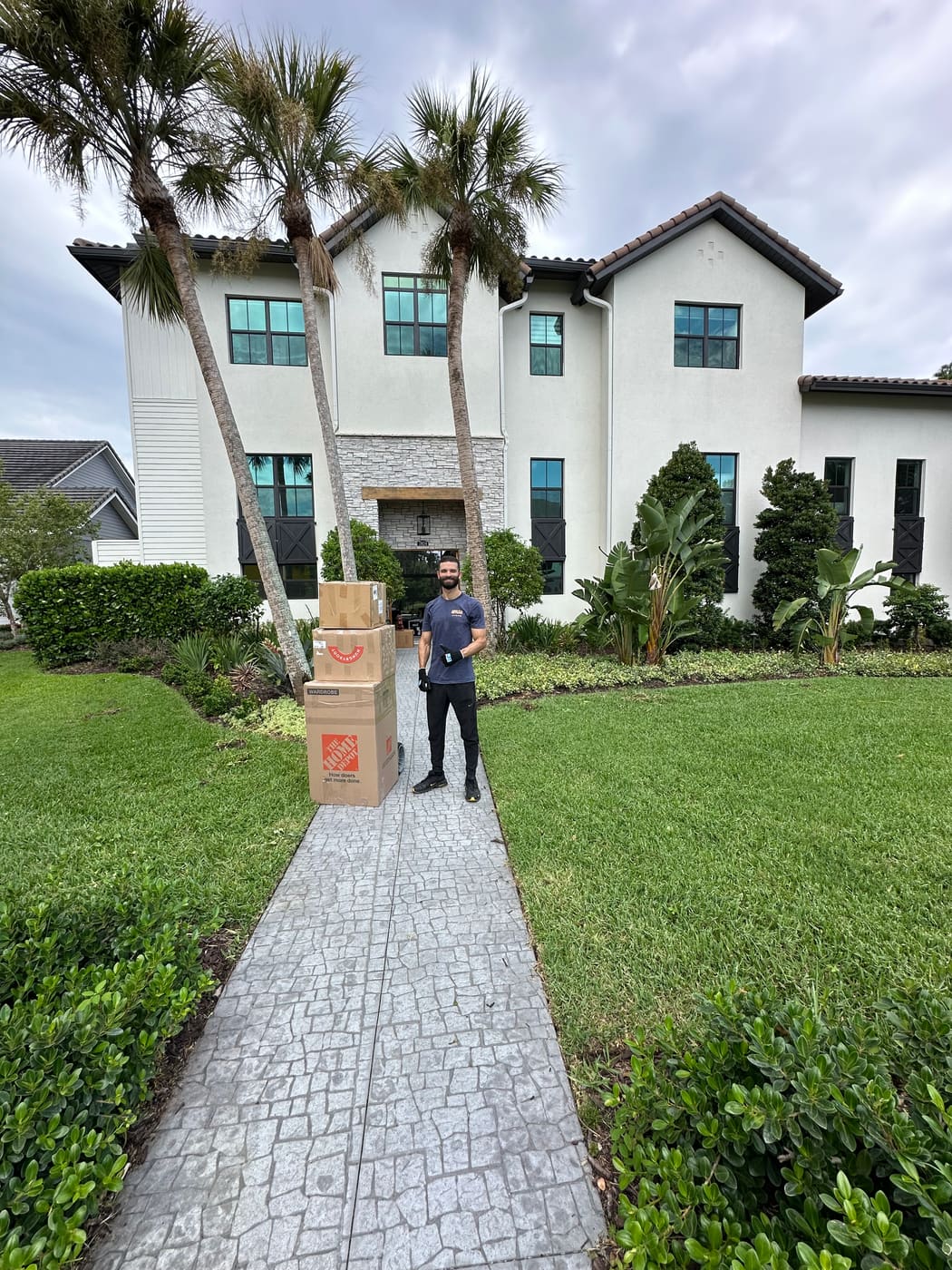 An Above&Beyond mover with a stack of packed boxes on a dolly at the front walk of a luxury home