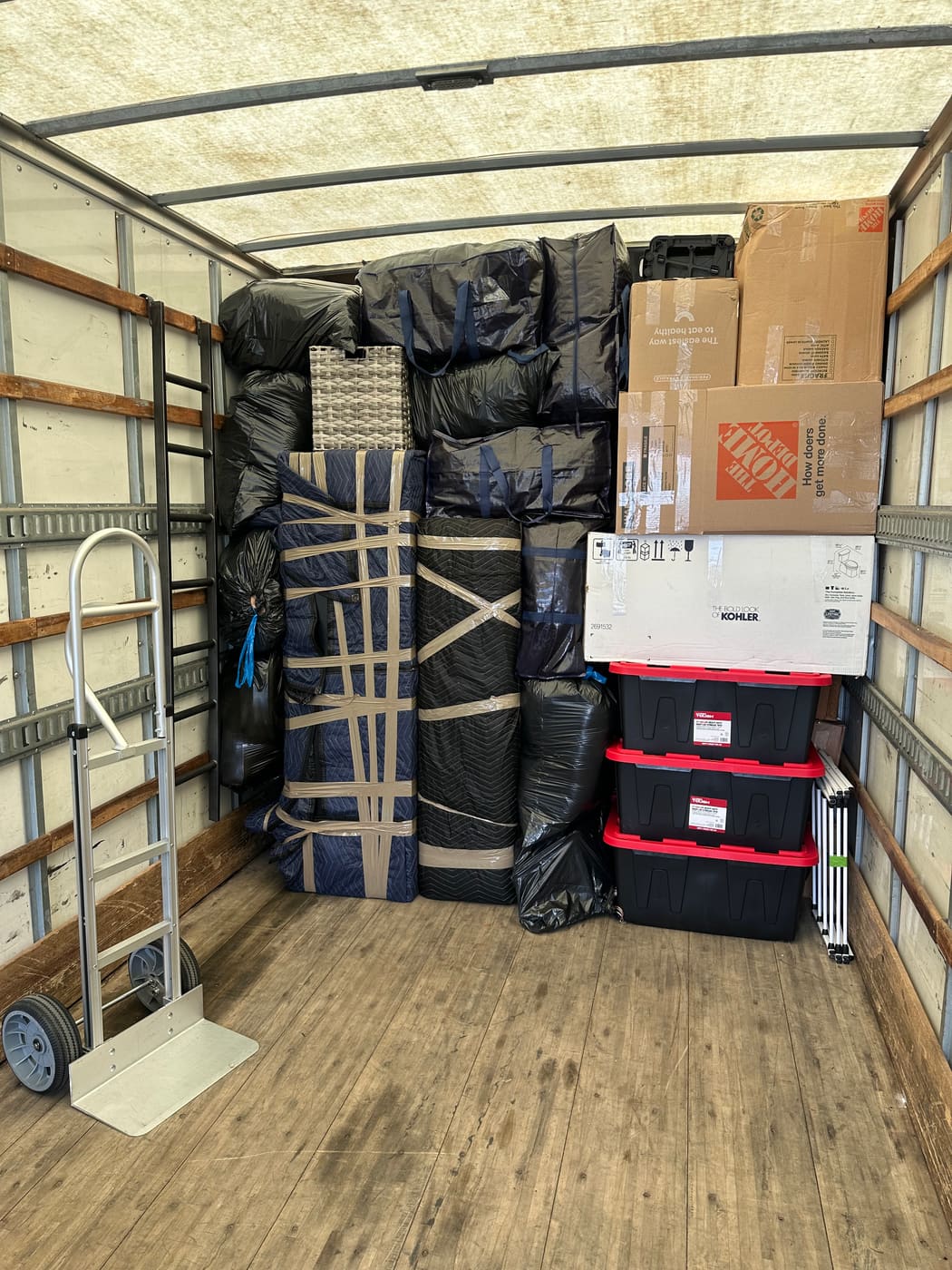 Truck interior packed wall to wall with strapped, blanket-wrapped furniture, boxes, and storage totes